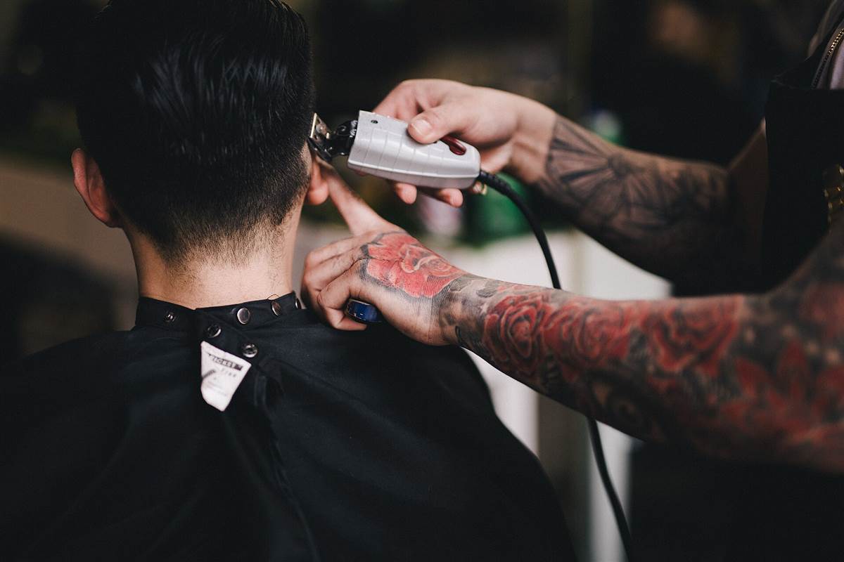 A barber trimming the back of a customer's neck with clippers