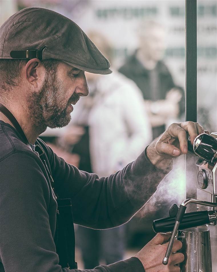 A barista in a flat cap working an espresso machine